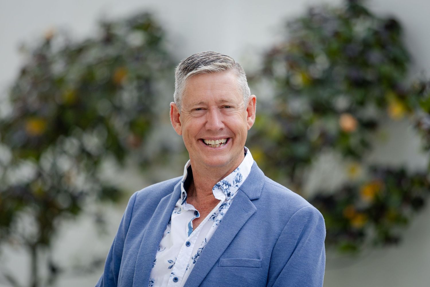 Professional portrait of someone in a blue blazer and patterned shirt outdoors.