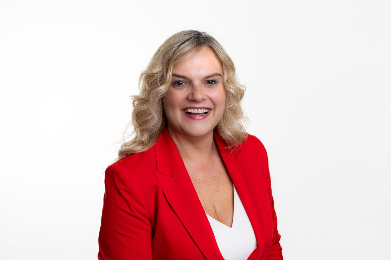 Professional portrait of someone wearing a bright red blazer and white top against a white background.