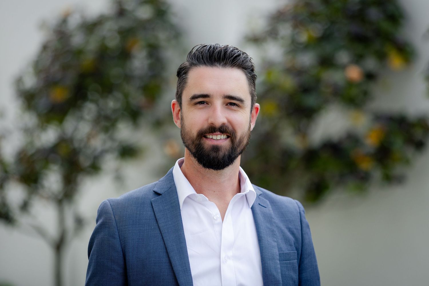 Professional headshot of someone in a navy suit jacket against a blurred background.