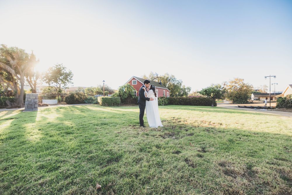 Bride and groom share a romantic embrace on a green lawn during their outdoor wedding ceremony.