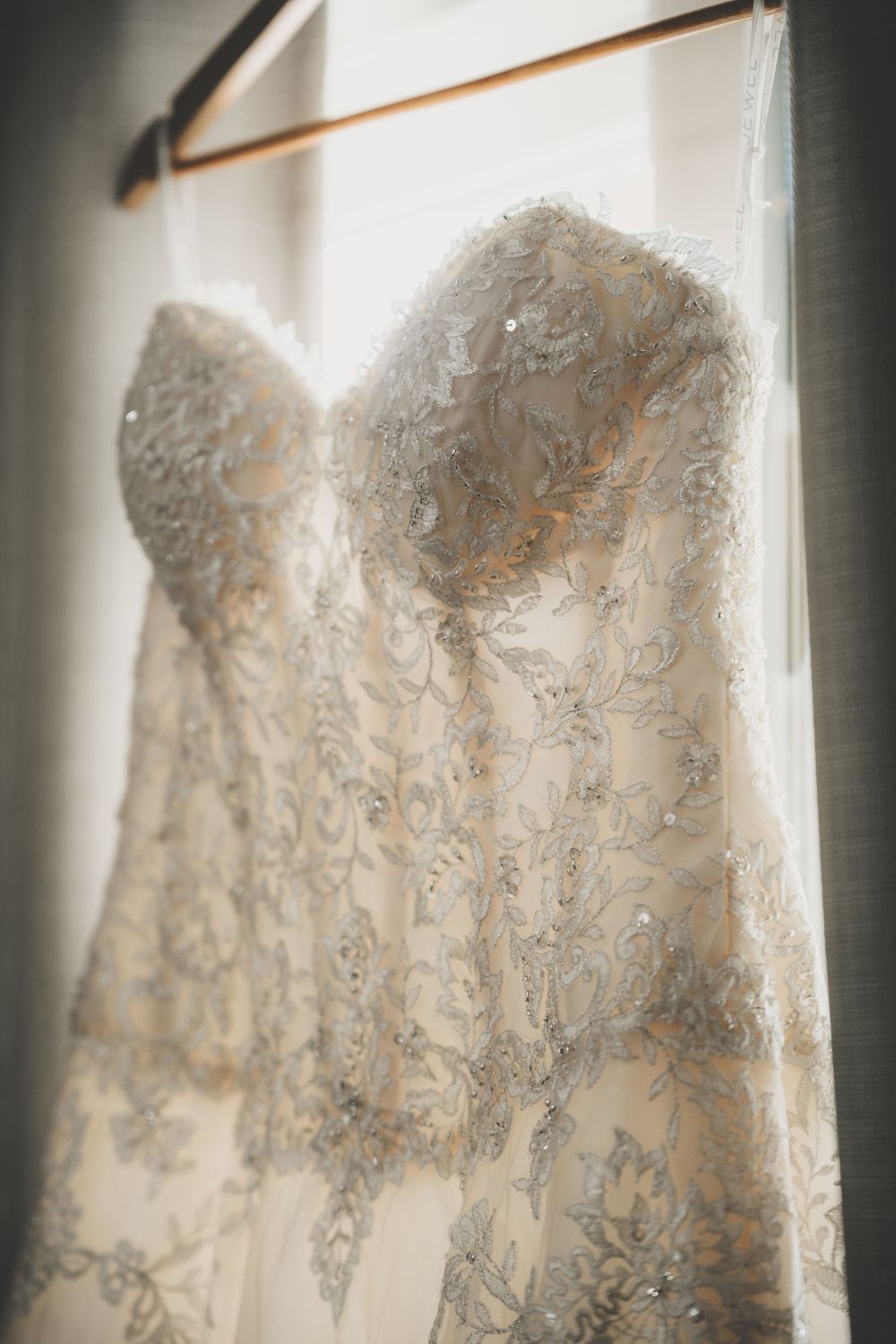 Close-up detail of intricate beaded lace bodice on strapless wedding gown hanging in window.