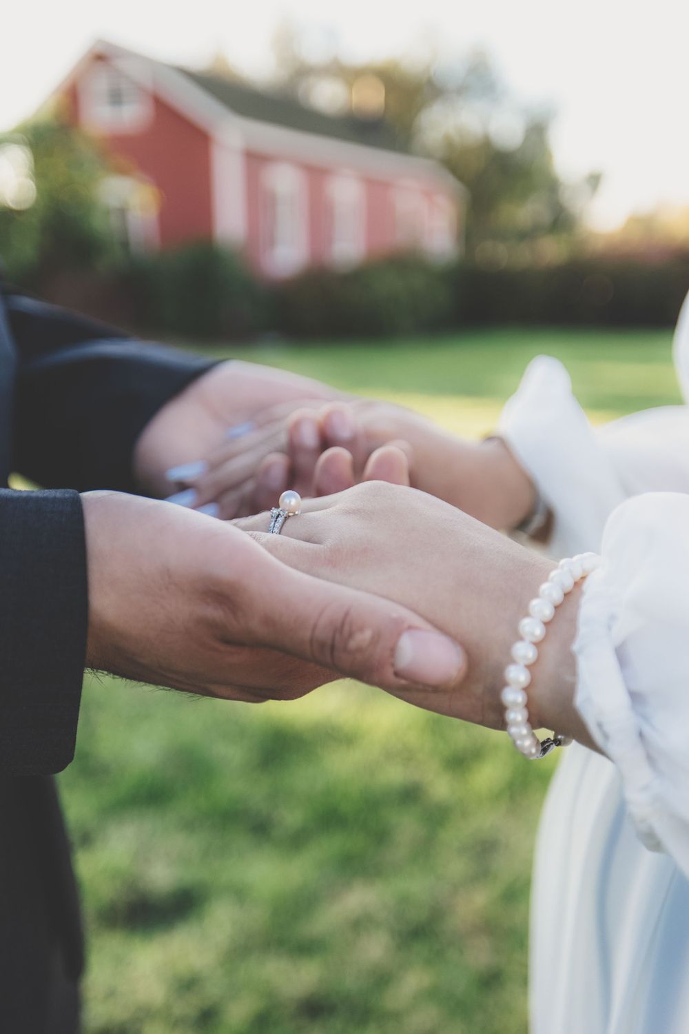 Close-up of bride and groom holding hands showing diamond engagement ring and pearl bracelet.