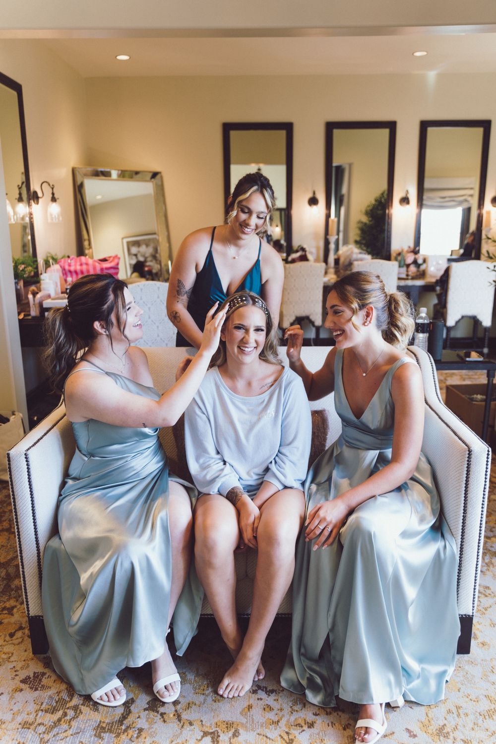 Bride smiling in robe surrounded by bridesmaids in blue dresses during wedding preparations.