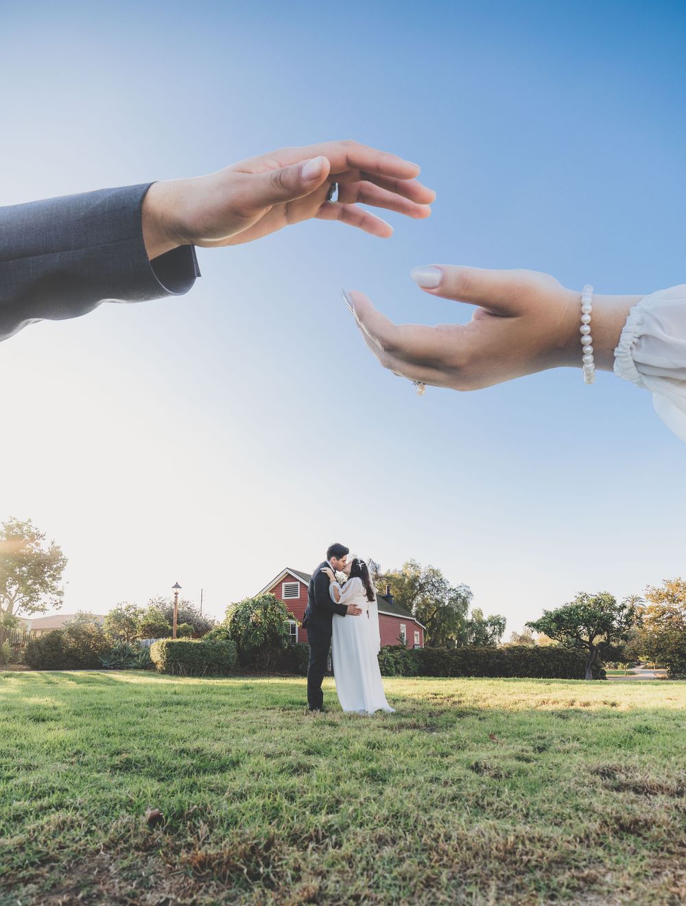 Creative perspective shot of bride and groom kissing on lawn framed by two hands overhead.