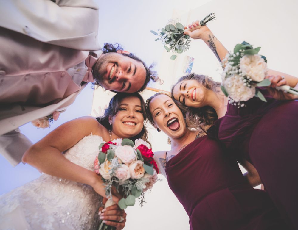 Low angle view of smiling bride and bridesmaids in burgundy dresses holding bouquets looking down.