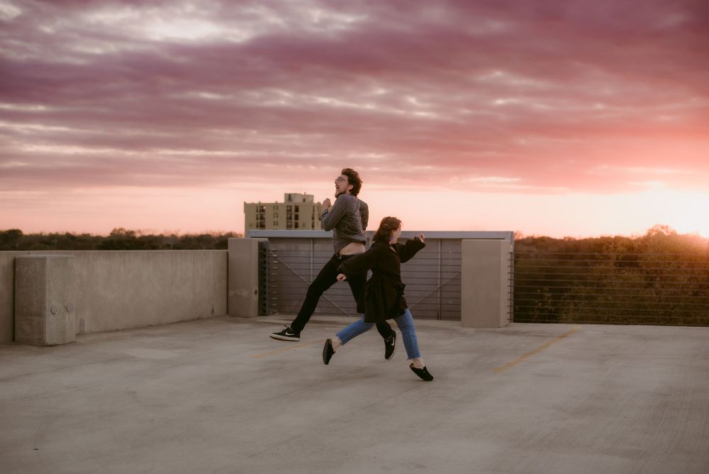 A Indie Couple Jumping Across a Rooftop during a Vibrant Pink Sunset in Seguin, Texas