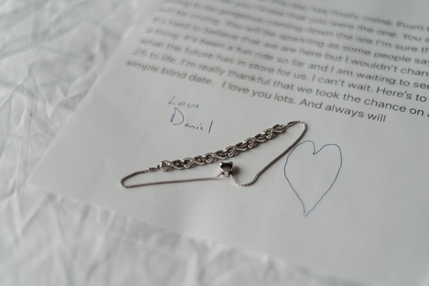 Delicate silver bracelet next to handwritten note with heart drawing.