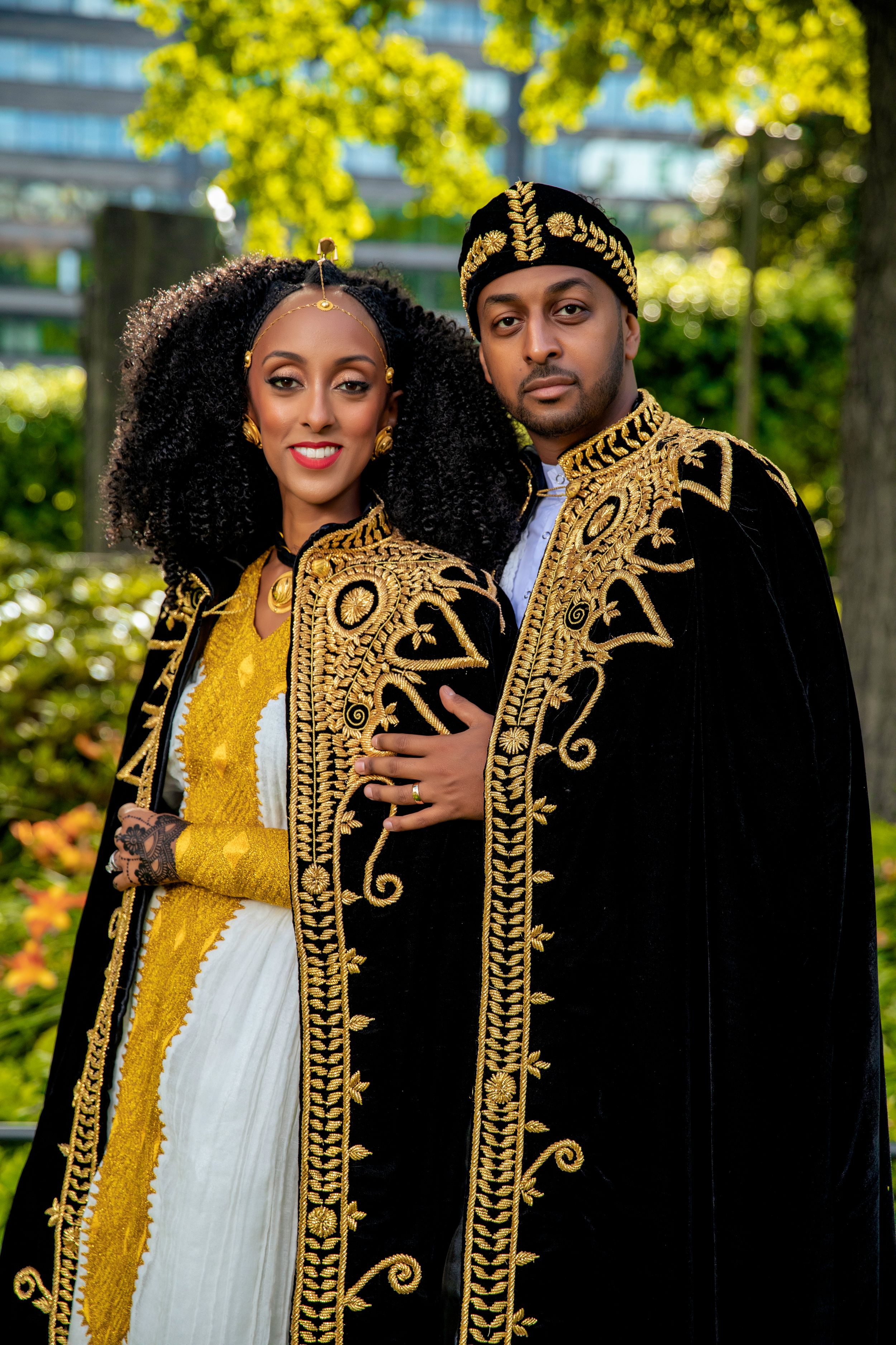 A couple wearing traditional Ethiopian formal attire with intricate gold embroidery designs.