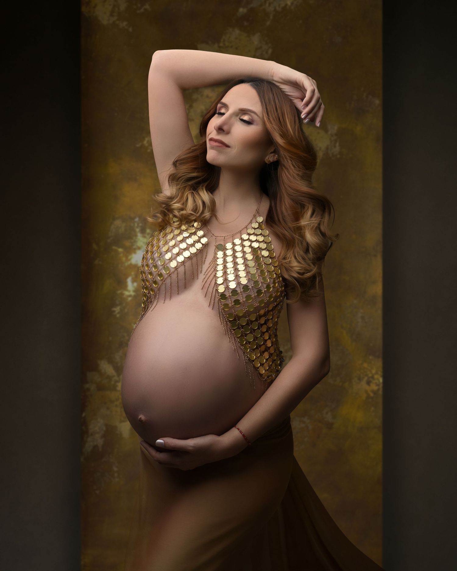 Artistic maternity portrait with golden metallic bodice against dark background.