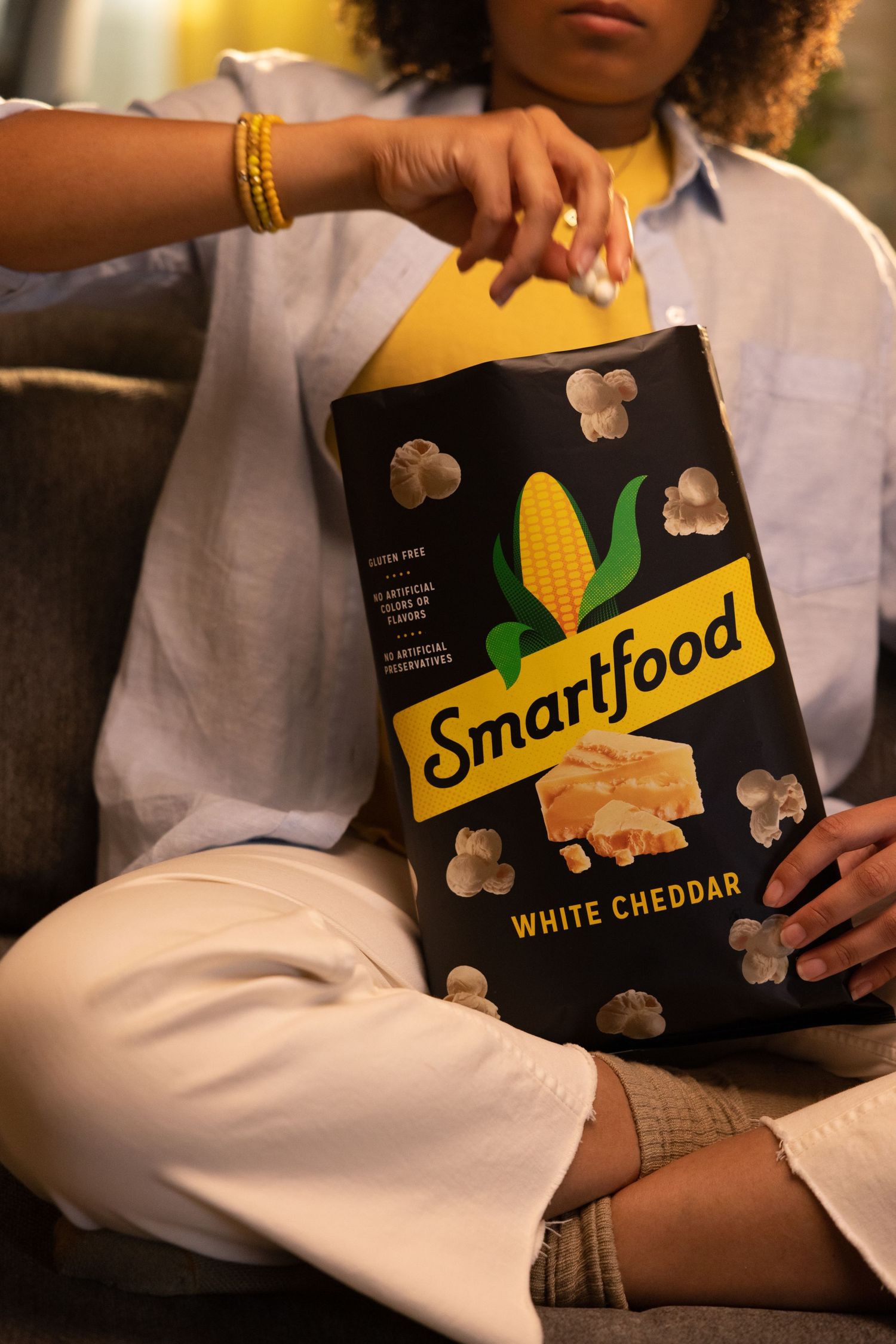 Hands holding Smartfood white cheddar popcorn bag against white background.