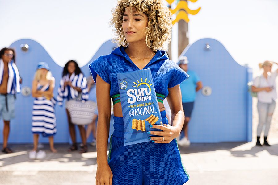 Person wearing blue shirt with curly hair standing outdoors near a blue wall.