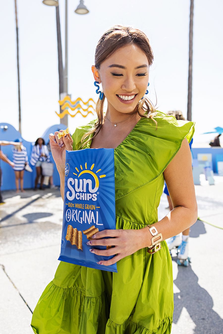 Person in bright lime green dress holding blue bag of Sun Chips outdoors.
