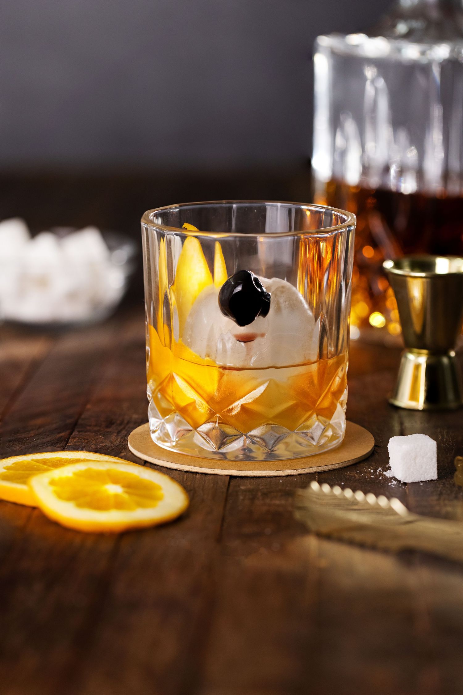 Old fashioned cocktail with orange garnish in crystal glass on wooden surface.