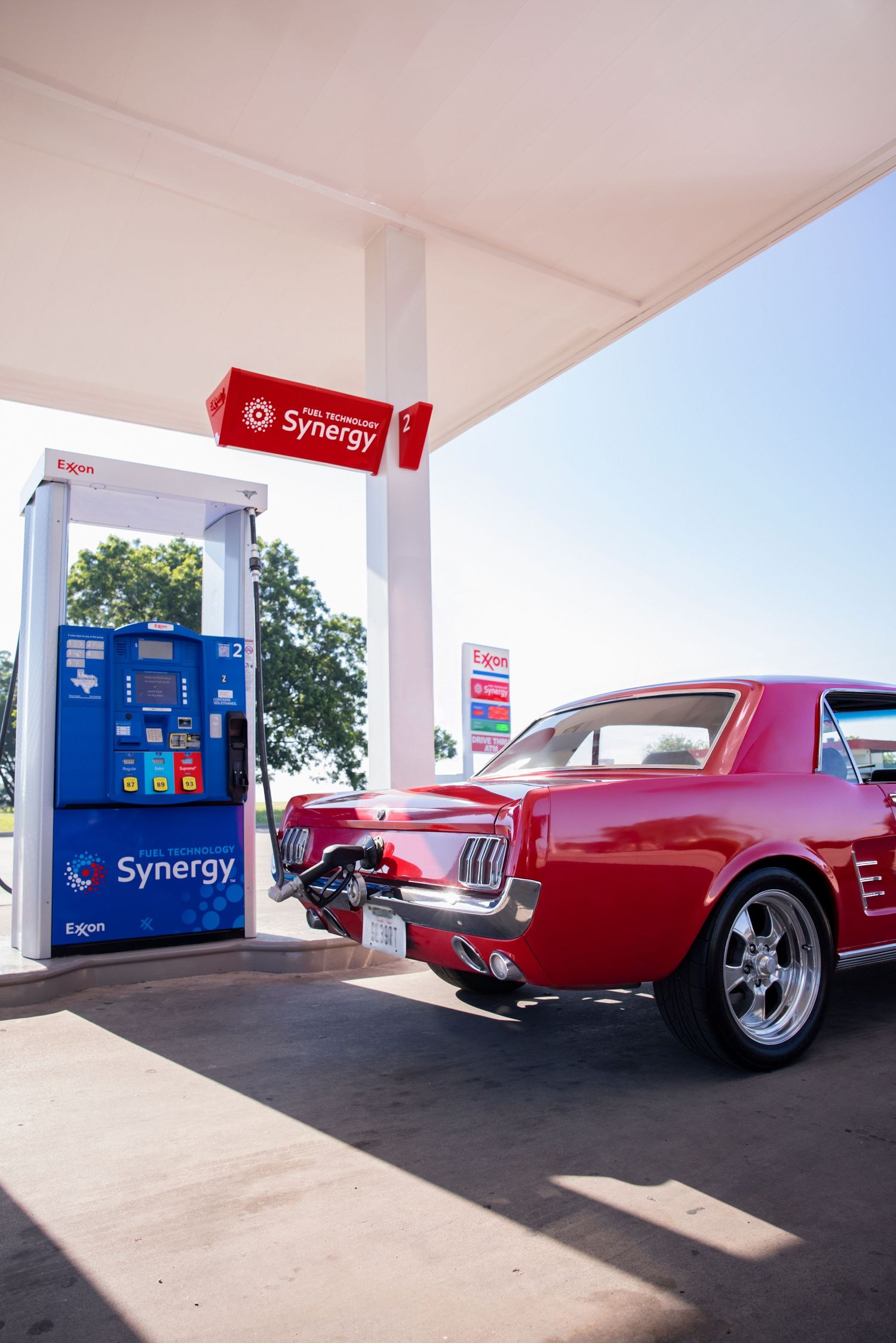 Red vintage car parked at a Synergy gas station with fuel pumps in view.