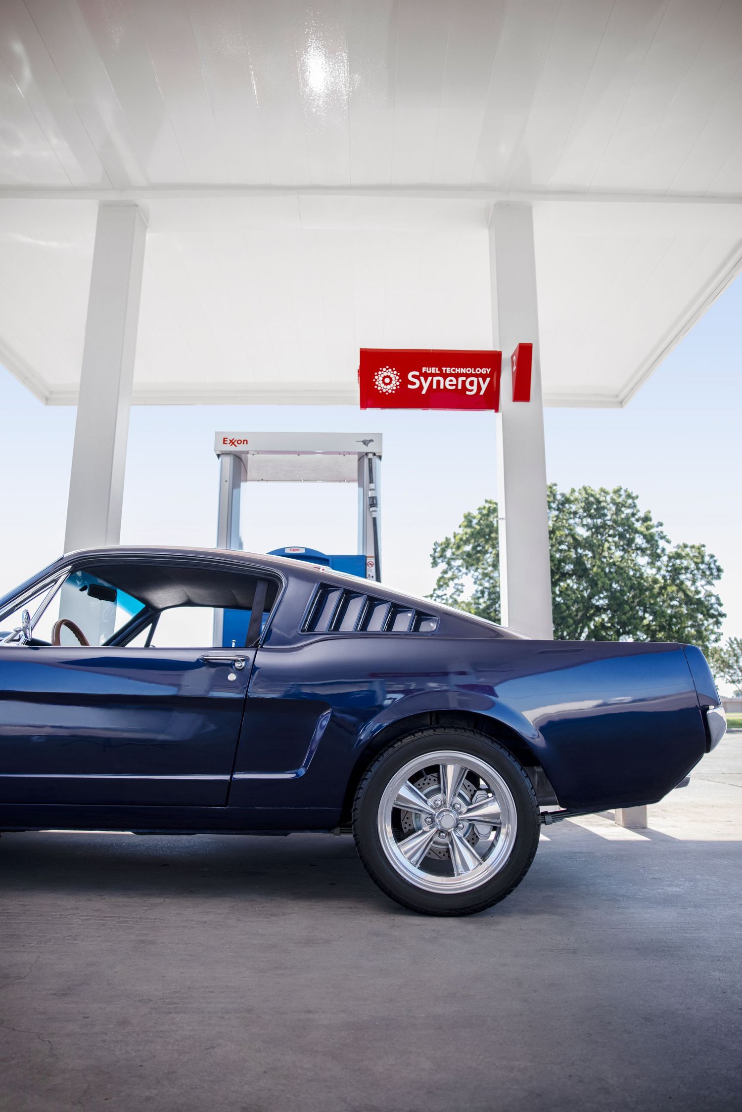 Classic blue muscle car parked under gas station canopy.