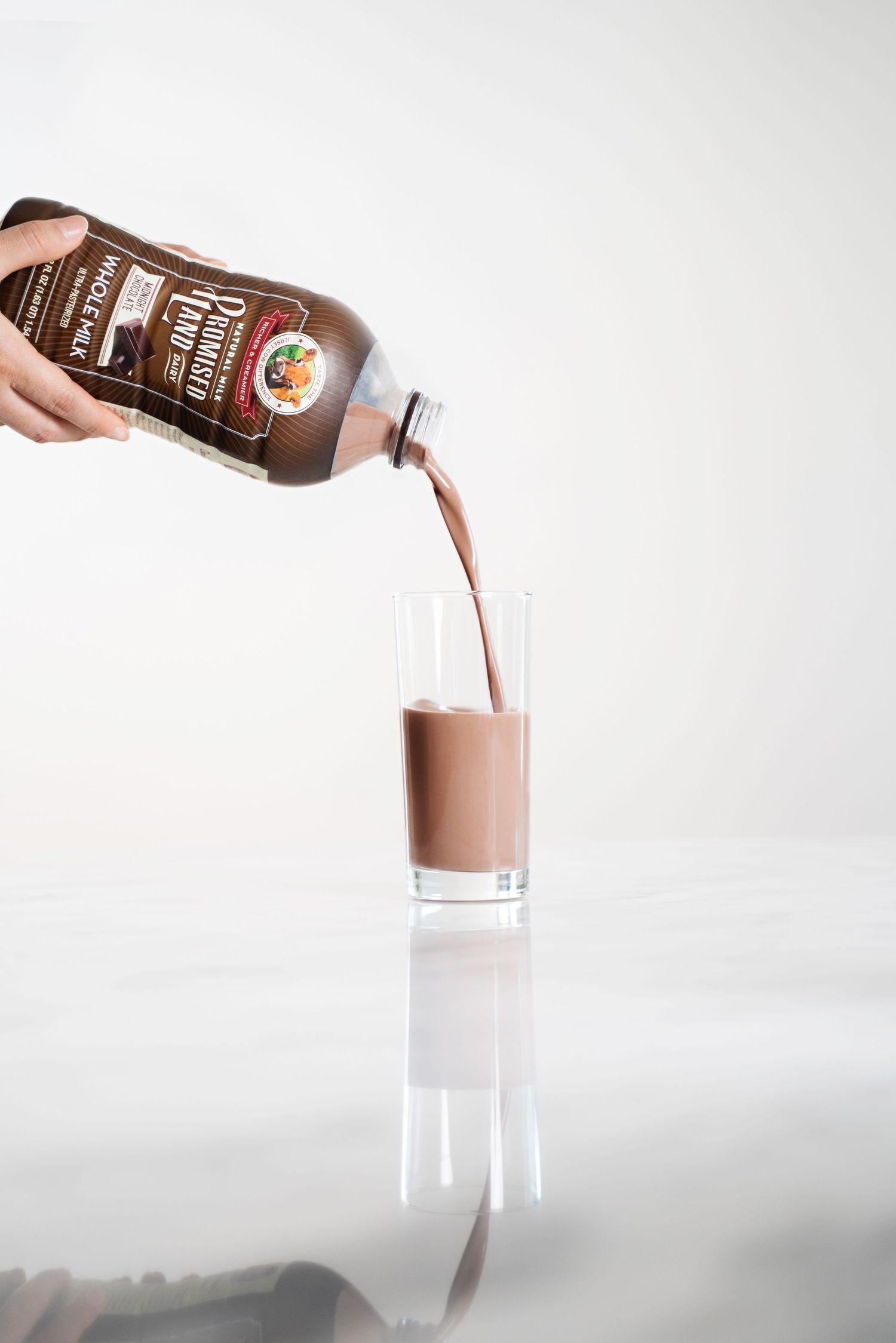 Chocolate milk being poured into a tall glass against a white background.