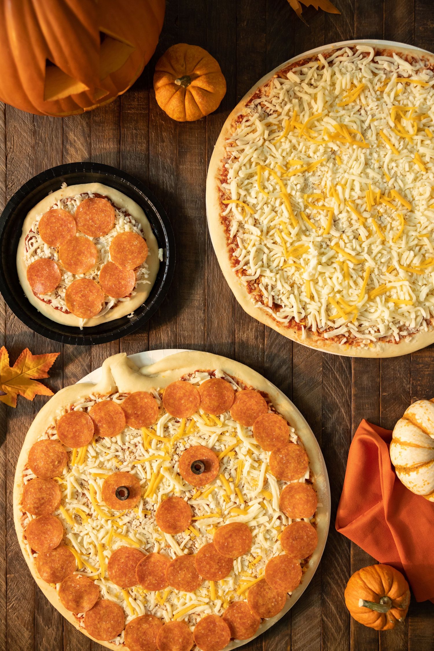 Halloween themed pizza decorated with pepperoni and cheese in a jack-o-lantern face pattern on dark wooden surface.