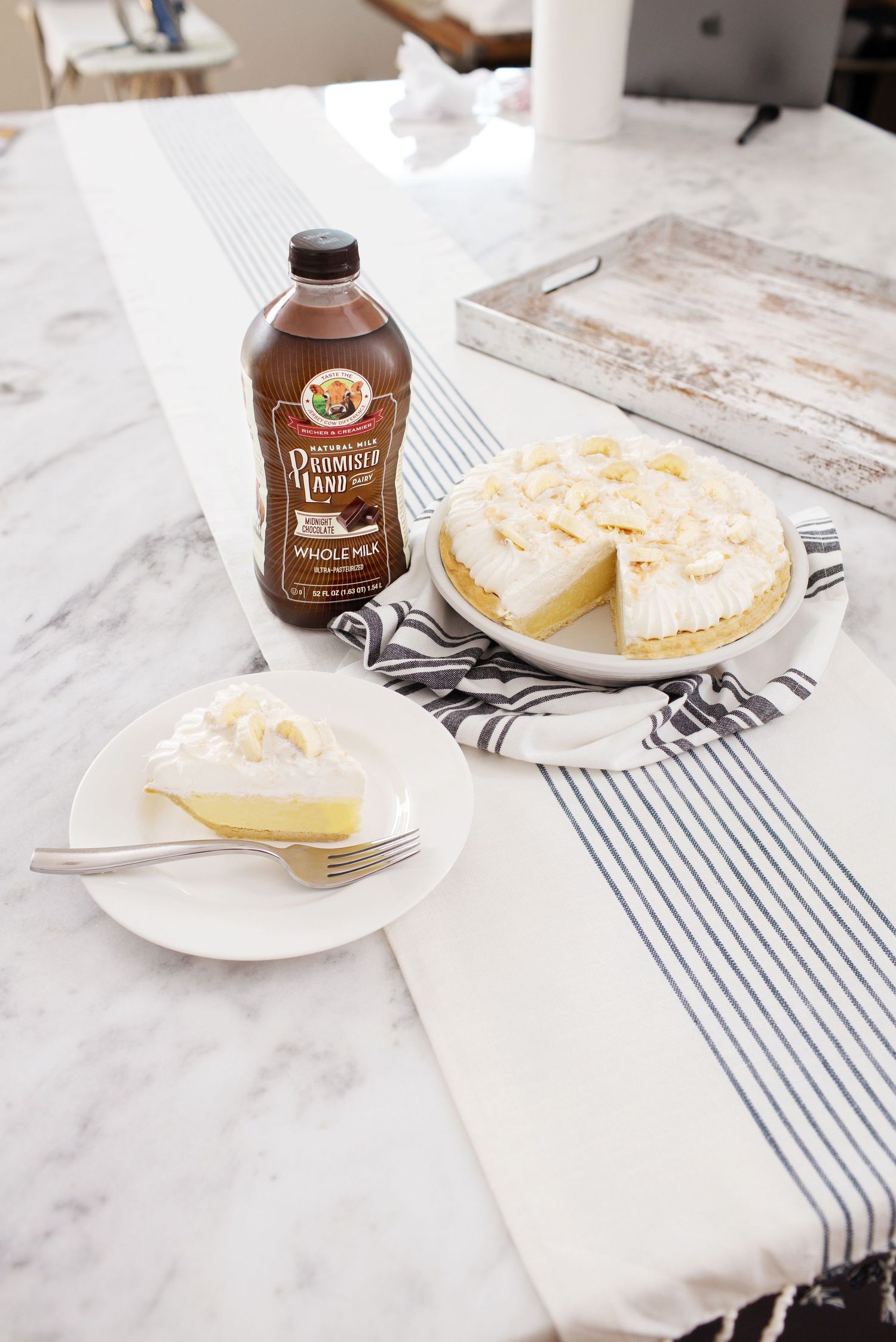 Lemon pie and chocolate syrup bottle arranged on marble countertop with striped napkin.