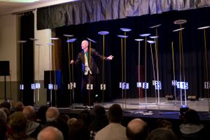 Performer on stage surrounded by tall spinning plates at a live show.