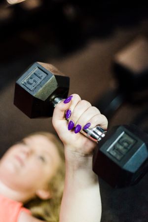Close-up of woman with purple nails lifting a 15lb dumbbell at the gym.