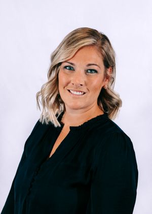 Professional blonde woman in black blouse posing for headshot on white background.
