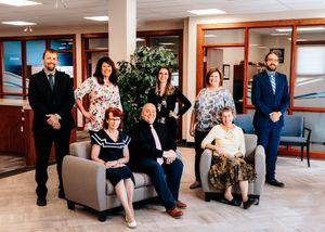 Group of nine professional office employees posing together in a modern office lobby.