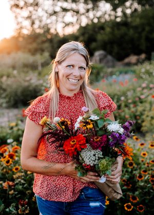 Smiling woman holding colorful bouquet in sunny flower garden at golden hour.