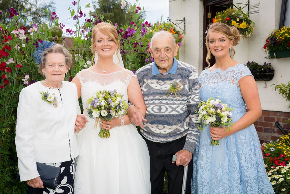 Wedding party poses in front of a garden with colorful flowers and hanging baskets.
