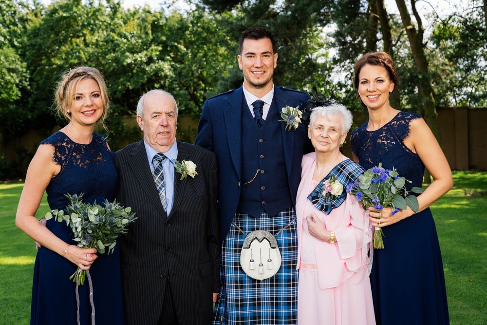 Wedding group photo with family members in formal attire standing together on a green lawn.