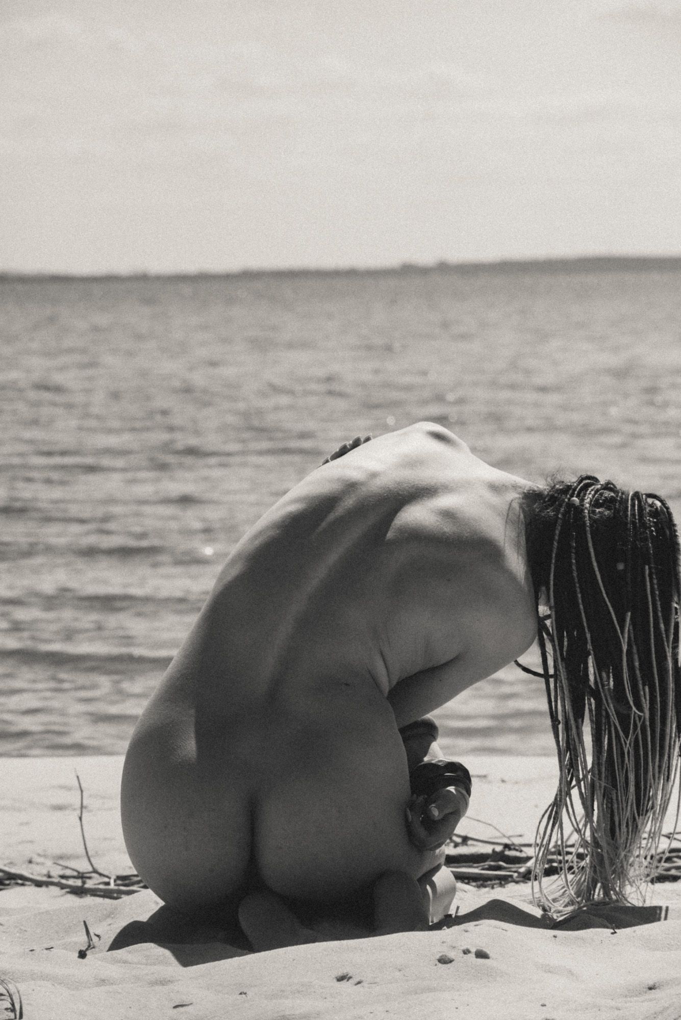 Black and white beach scene with artistic nude figure on sandy shore.