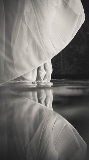 Ethereal black and white photos of flowing white fabric reflecting on glossy surface.
