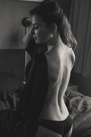 Artistic black and white boudoir photo showing bare back against dark background.