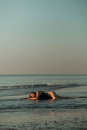 Figure lying in shallow ocean water at sunset creating reflective silhouette.