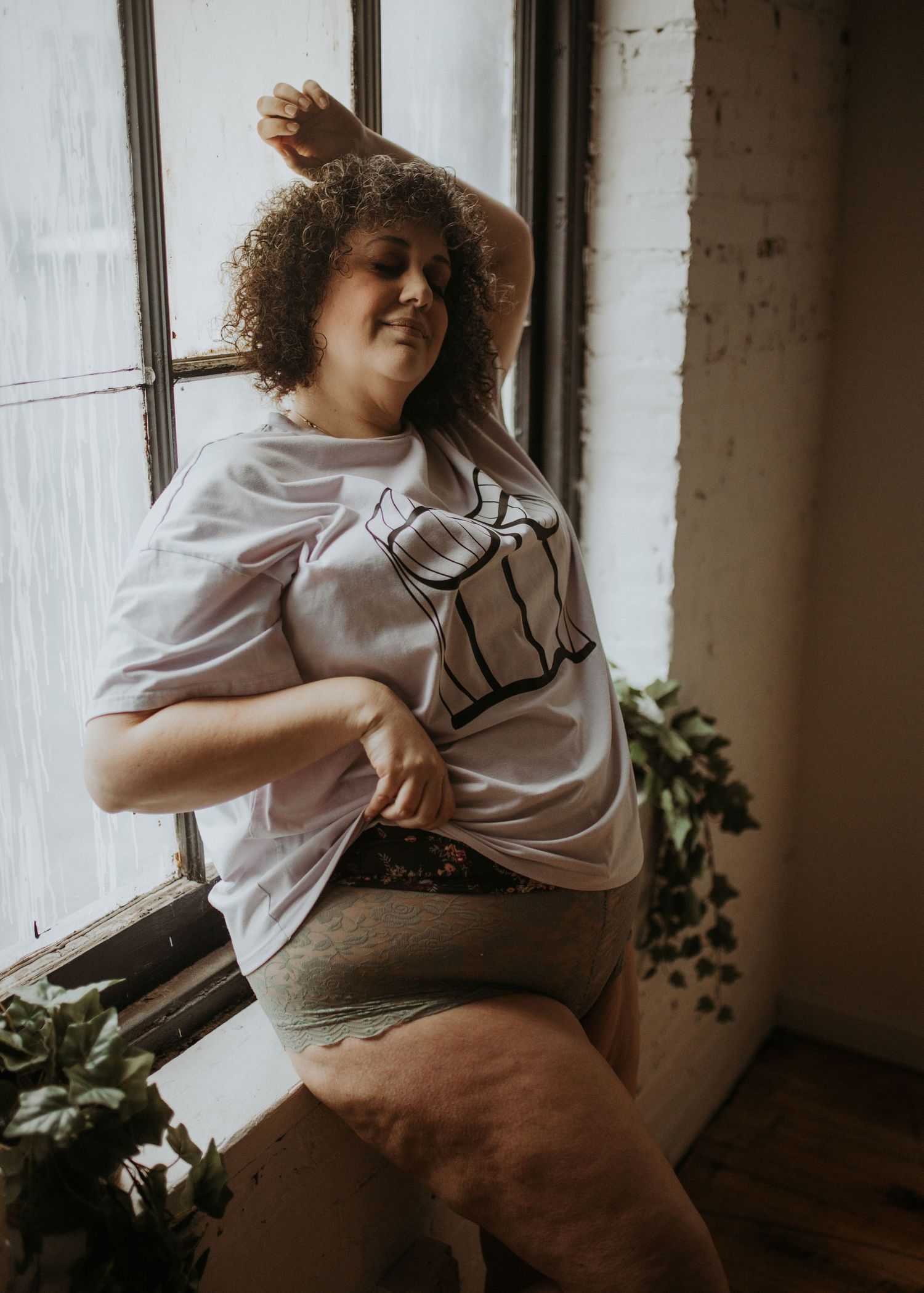 A person in a white t-shirt dances joyfully by a window with natural light streaming in, surrounded by houseplants.