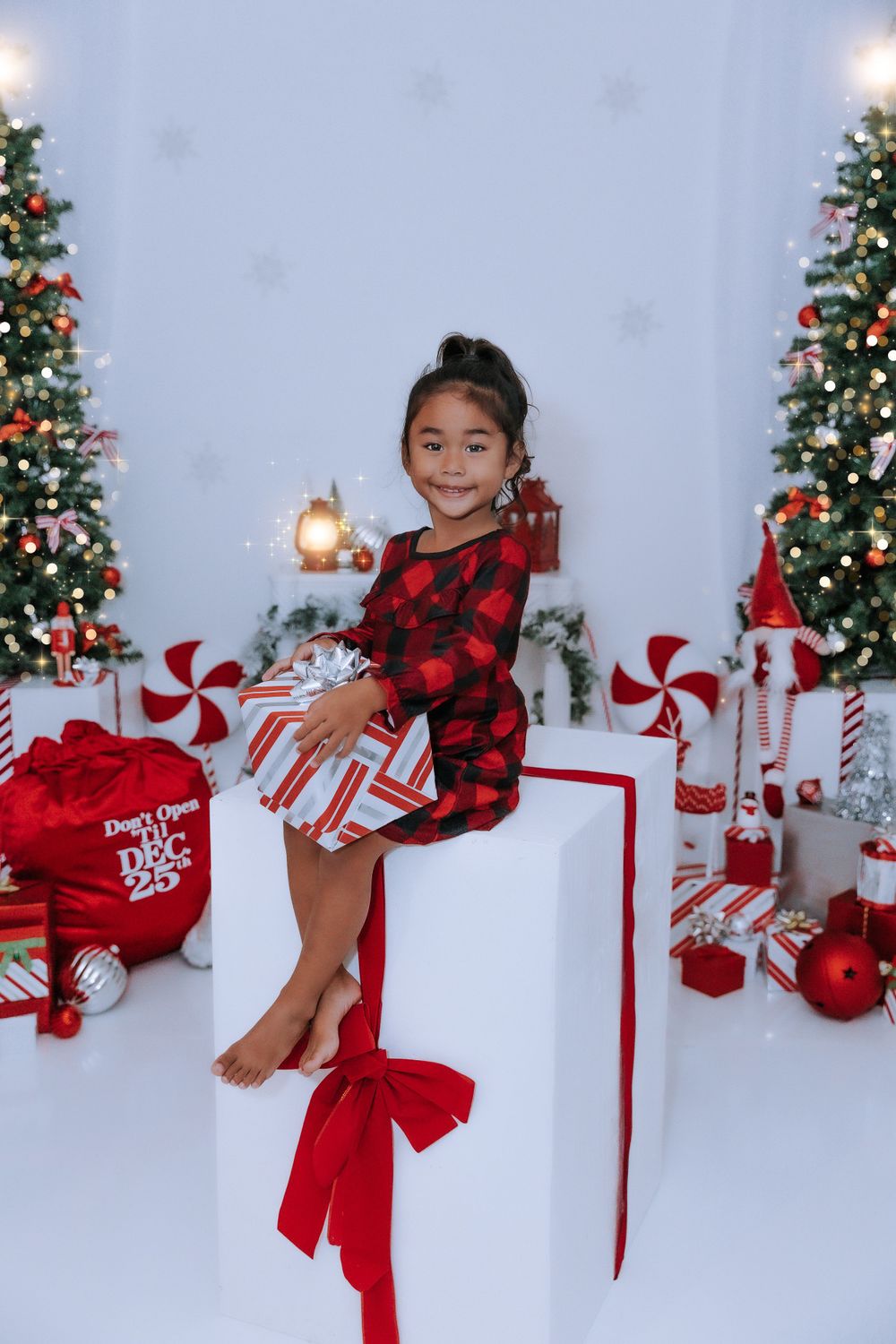 A festive Christmas photo setup with a decorated tree, red and white peppermint decor, and wrapped presents.