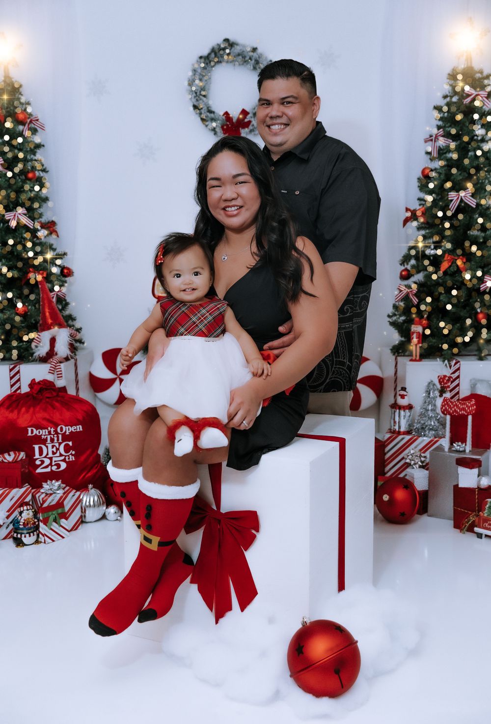 Family posing in front of Christmas decorations with red and white holiday theme.