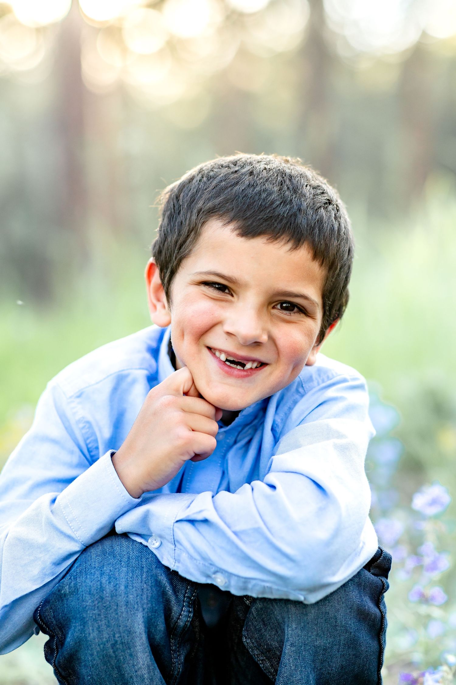 Young boy squats and leans his face on his hand, smiling, during their family session in Colorado Springs.