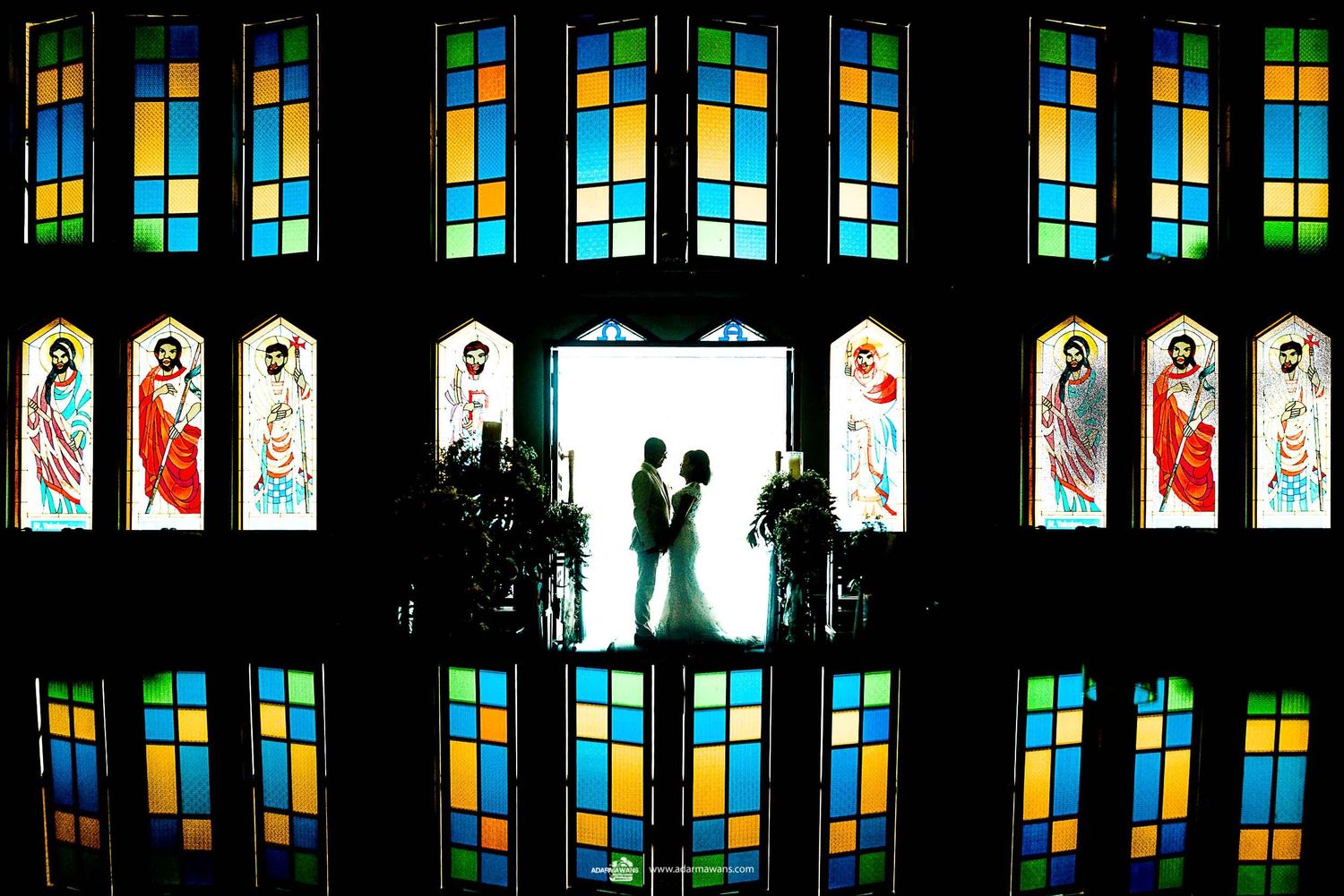 Silhouettes against colorful stained glass windows in church.