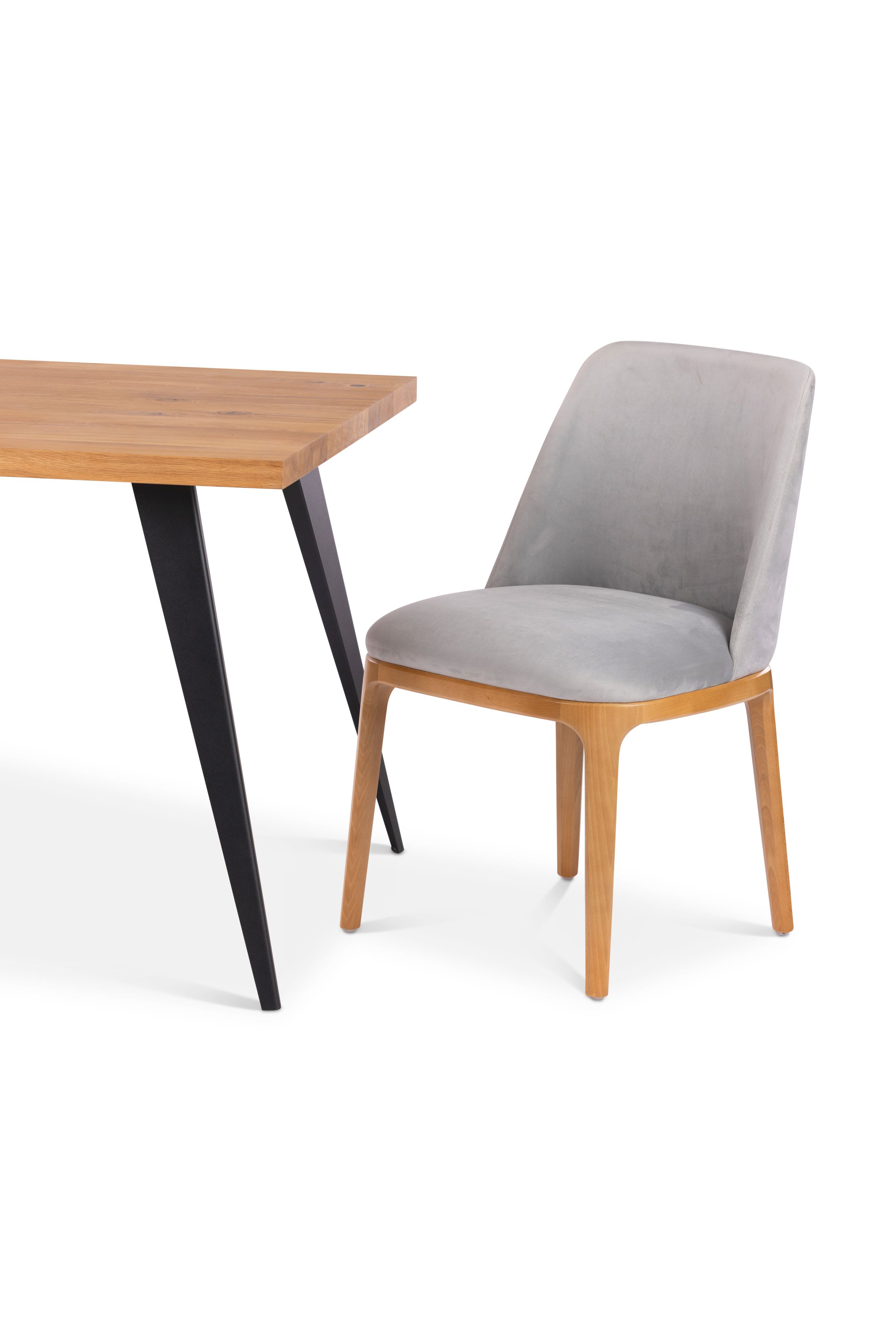 Contemporary dining chair with grey upholstery and wooden frame next to table with black legs.