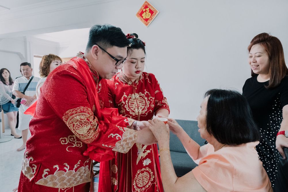 A couple in traditional red Chinese wedding attire accepts tea during a tea ceremony with family members.