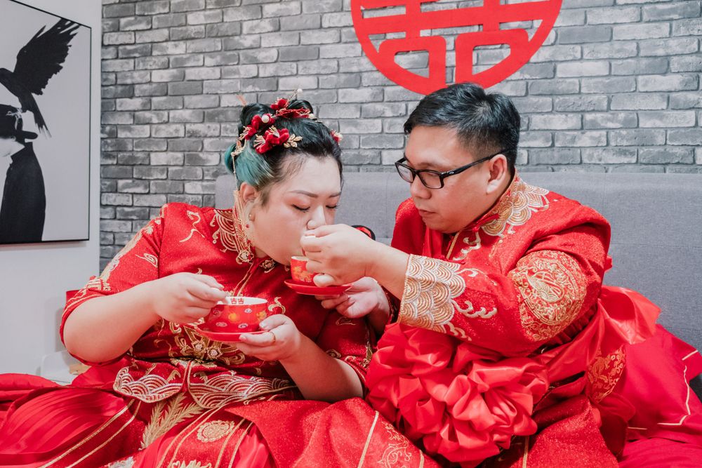 Couple in traditional red Chinese wedding attire sharing tea.