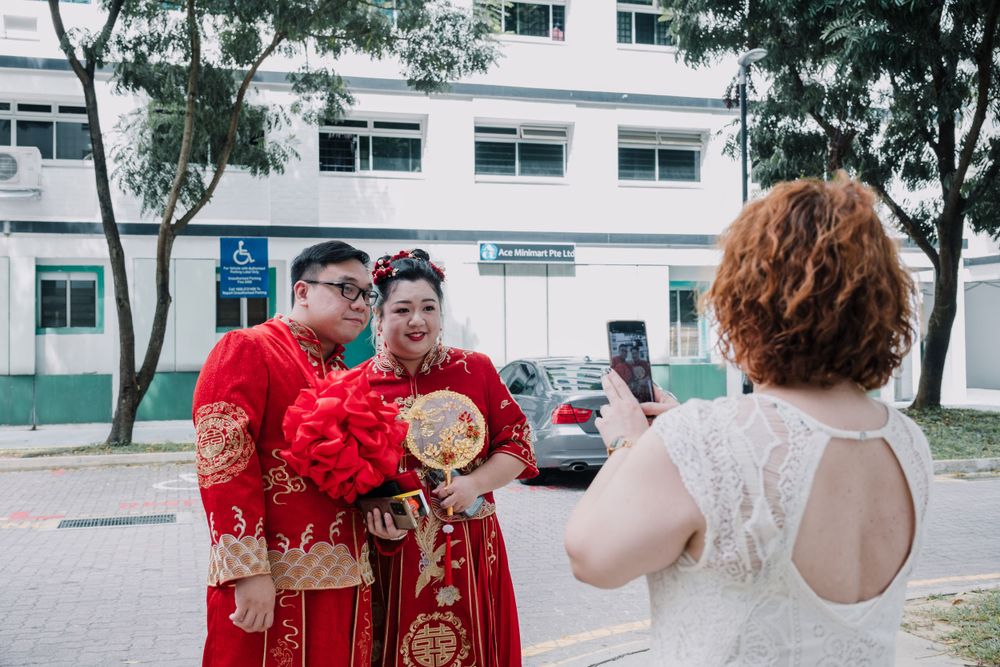 A couple in red traditional Chinese wedding outfits poses for photos outdoors.
