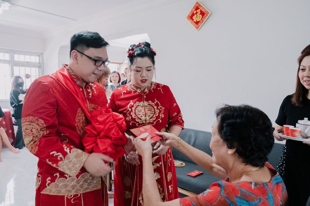 A couple in red traditional Chinese wedding outfits participates in a tea ceremony ritual.