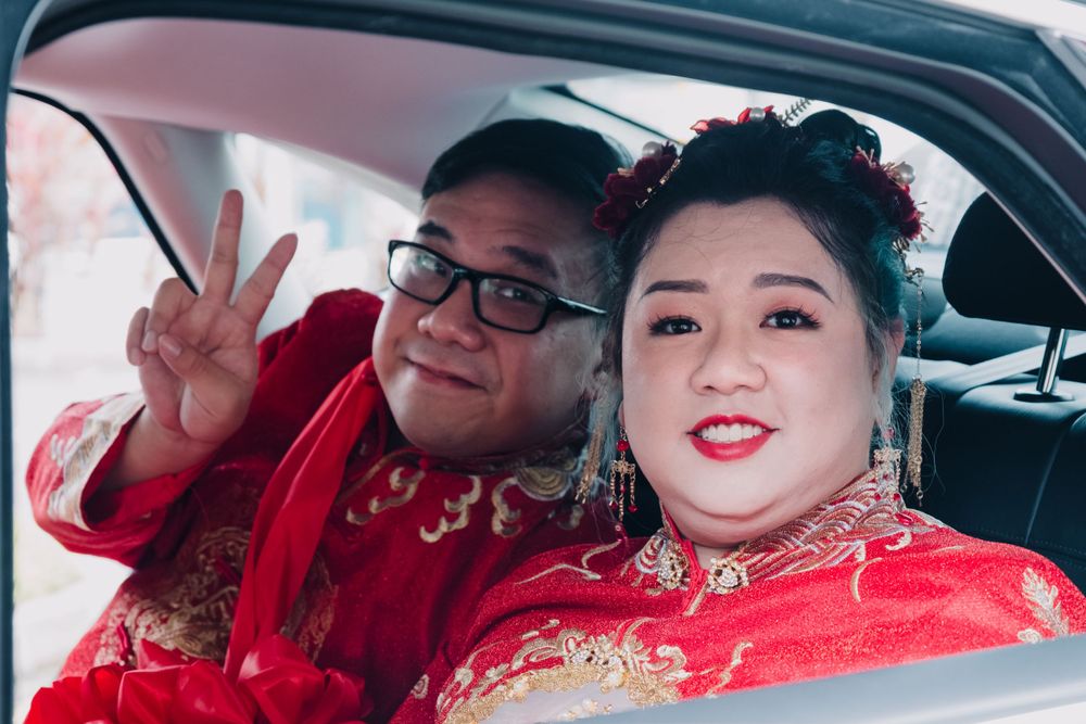 A couple dressed in traditional Chinese wedding attire pose in a car.