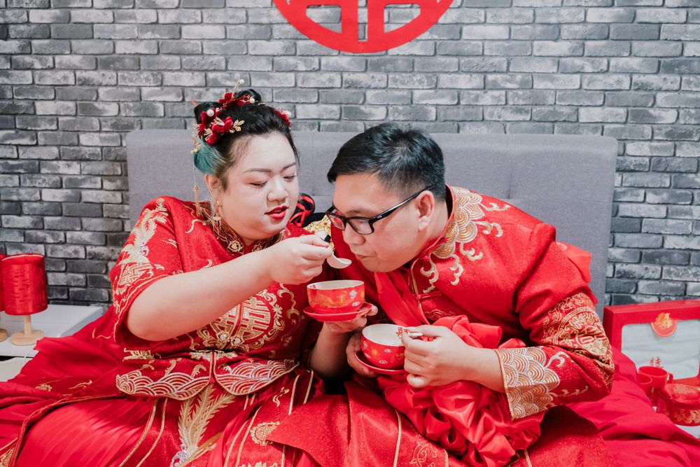 Newlyweds in red traditional Chinese outfits drinking tea together.