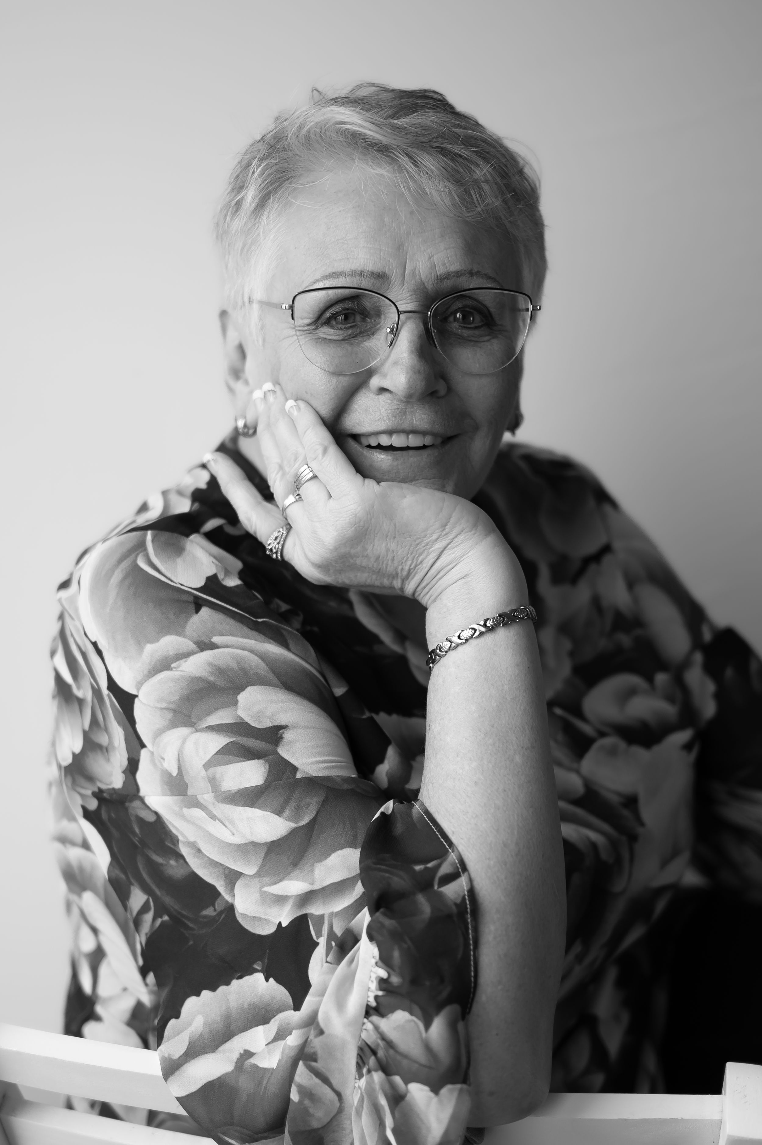 Black and white portrait of a person in floral print resting their head on their hand.