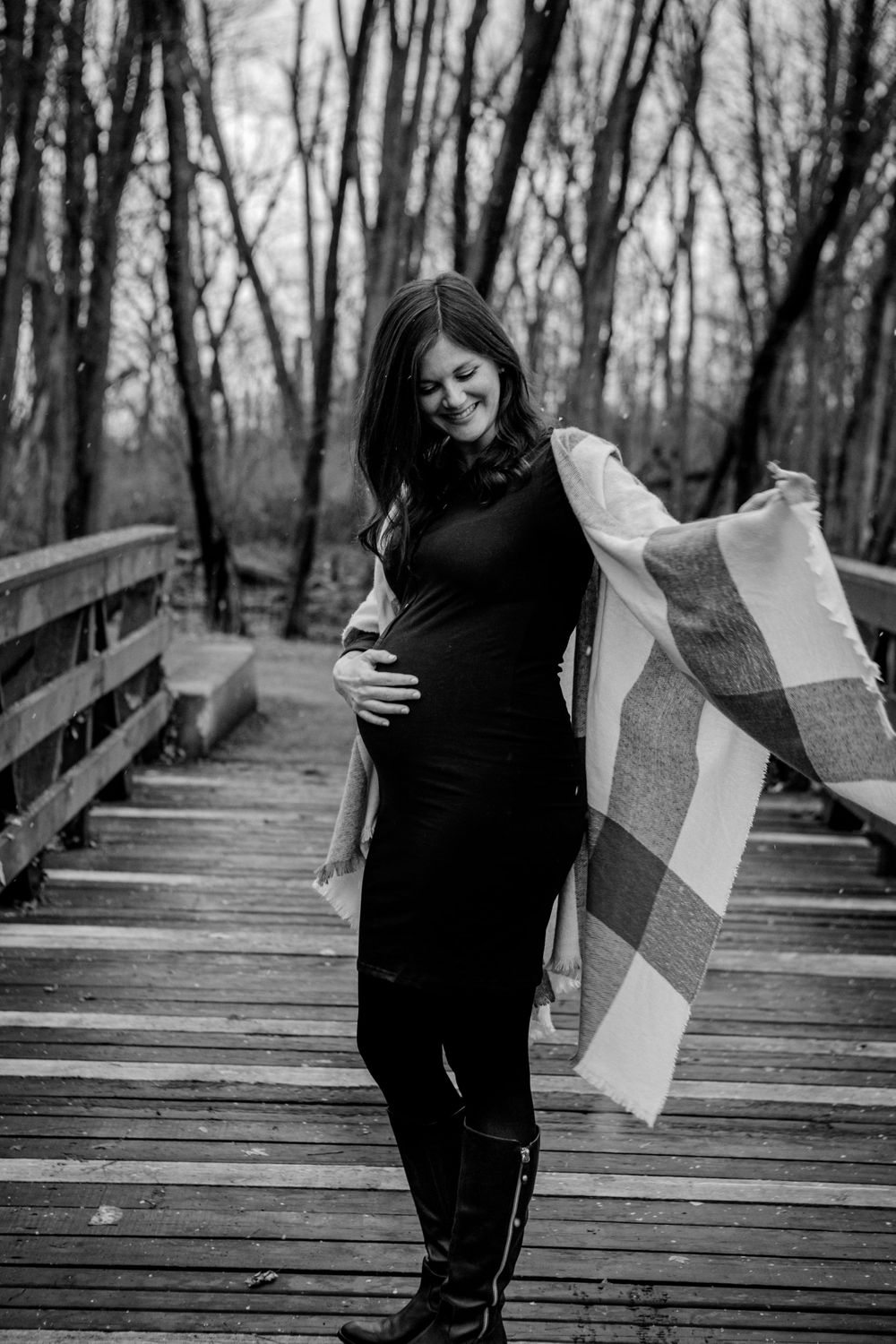 Black and white maternity photos on wooden bridge with flowing scarf.