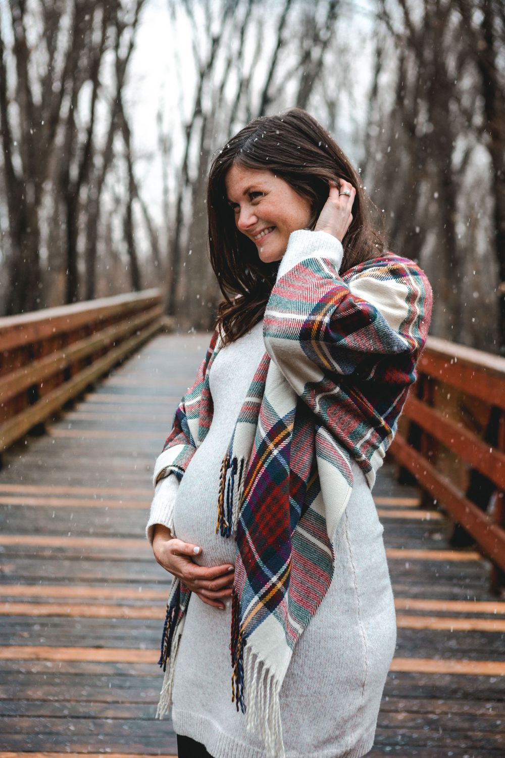 Maternity photoshoot on wooden bridge with plaid scarf in winter setting.
