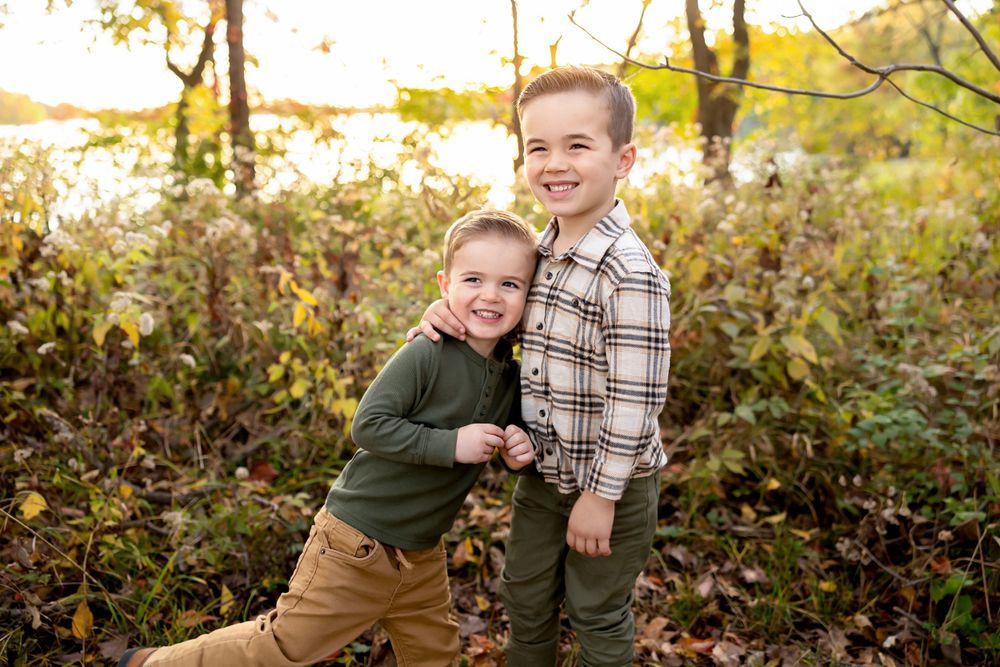 Two children playing and laughing together in front of fall foliage.