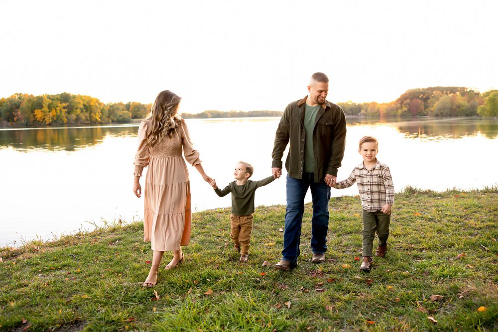 A family holding hands and walking together by a serene lake at sunset.